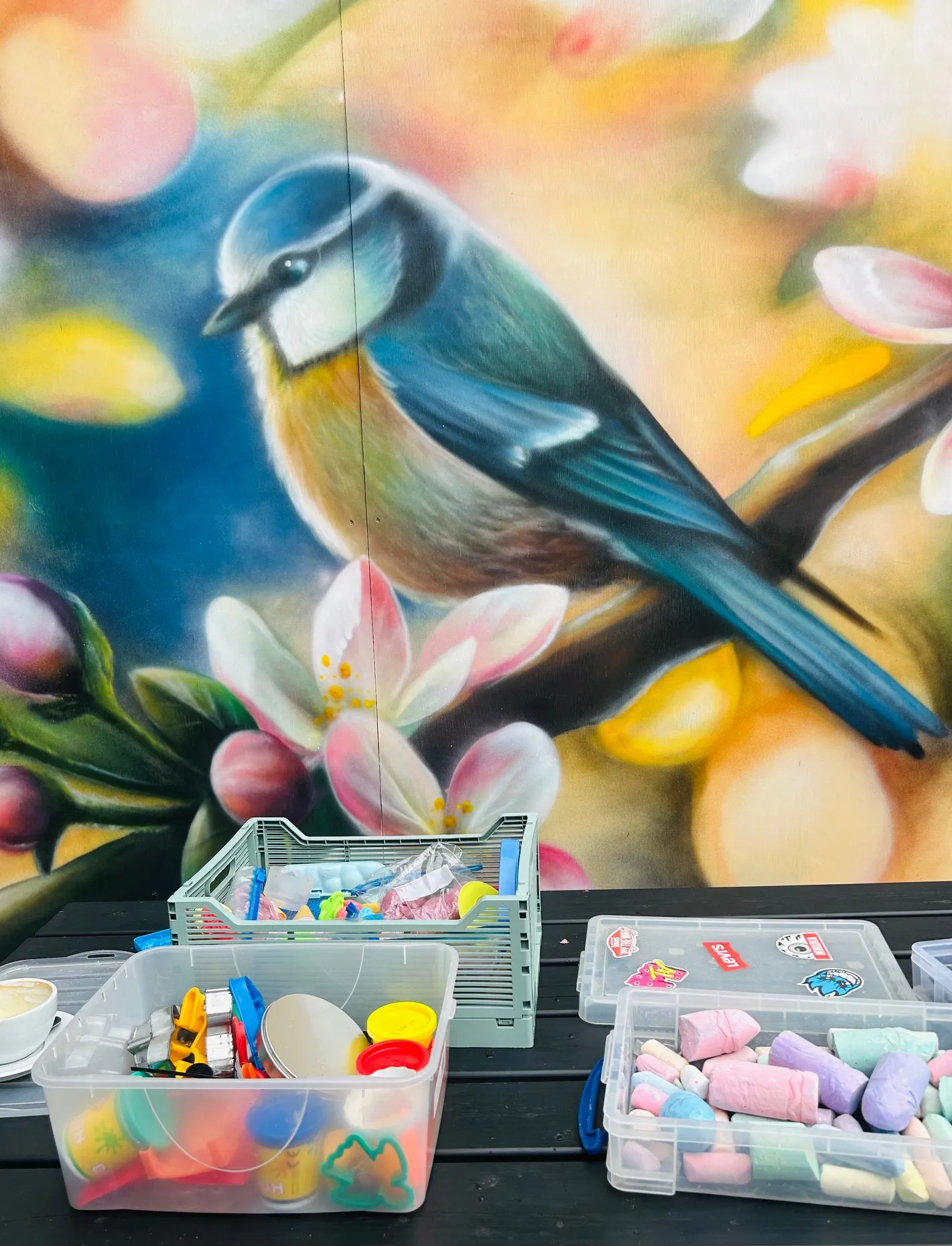 A hand-painted blue tit mural on the wall of The Yard, above a table of craft and chalk boxes