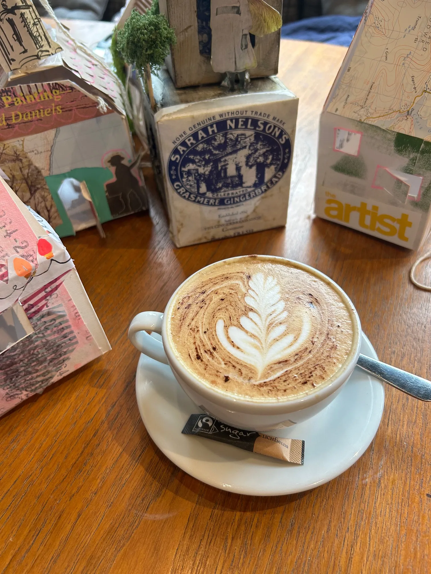 A cappuccino with latte art on a wooden cafe table, surrounded by vintage art books and collage materials