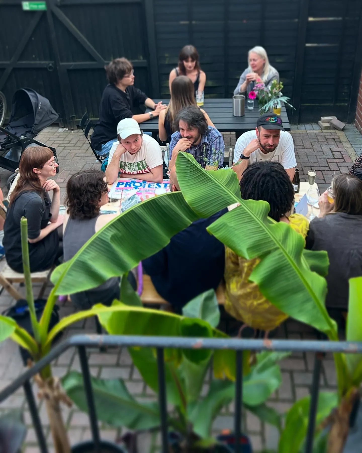 Guests relaxing around tables in The Yard, Art Club's secluded outdoor garden, framed by banana plants